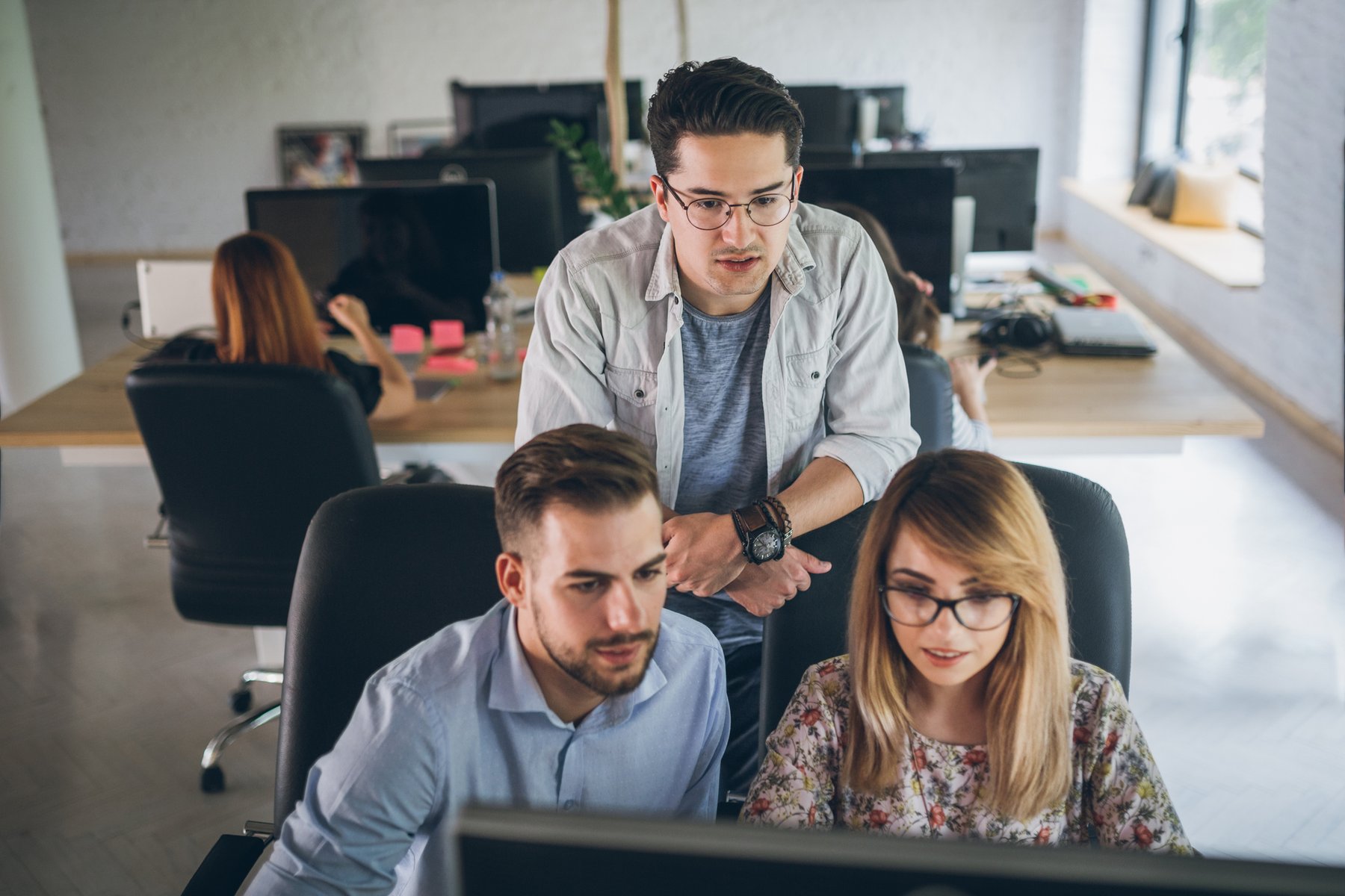 Three people collaborating at computers in a shared office